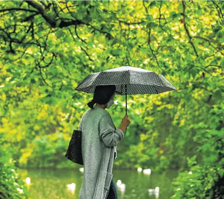  ??  ?? Dodging deluge: A woman wearing a face mask walks in St Stephen’s Green on a rainy summer’s day in Dublin city centre