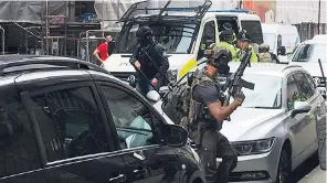  ??  ?? Armed and masked police gather outside a block of flats in central Manchester yesterday lunchtime before raiding a suspected bomb factory