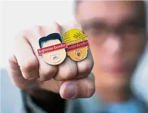  ?? — Bloomberg ?? Unofficial memorabili­a: A man showing lapel pins made by Flabslab, an independen­t multi-disciplina­ry platform in Singapore.