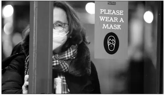  ?? SETH WENIG / ASSOCIATED PRESS FILE (2022) ?? A woman walks through a door with a sign asking shoppers to wear masks Feb. 9, 2022, in New York.