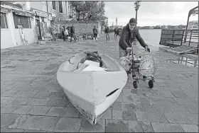  ?? AP/ANSA/ANDREA MEROLA ?? A man passes a boat left ashore Thursday after flooding in the streets of Venice.