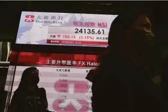  ?? Vincent Yu / Associated Press ?? People pass an electronic billboard beaming the results of a dismal day at the Hong Kong stock exchange. Shares fell more than 3% Monday, part of a sell-off that swept global markets.