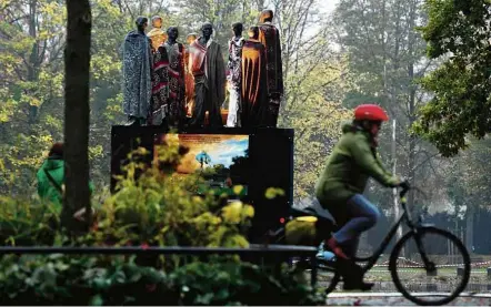  ?? Patrik Stollarz/AFP ?? Durante Conferênci­a do Clima na Alemanha, ciclista passa em frente à estátua em homenagem a refugiados climáticos