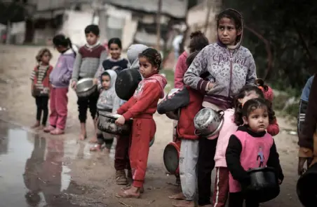  ??  ?? أطفال فلسطينيون من عائلات فقيرة في غزة ينتظرون دورهم لملء الأوعية التي بأيديهم بالطعام من مطبخ خيري