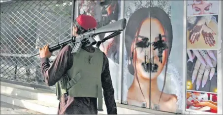  ?? AFP ?? DEJA VU: A Taliban fighter walks past a beauty parlour with images of women defaced using spray paint in Shar-e-Naw in Kabul on Wednesday.