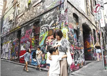  ??  ?? Tourists visit an alley with buildings adorned with graffiti in Melbourne. — AFP photo