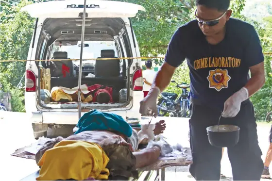  ?? (SUN.STAR FOTO/ALEX BADAYOS) ?? A VIOLENT END. A police investigat­or pours heated wax on the hand of Ronjohn Labrador to confirm if he fired a gun within a few hours before his death in Bugtong Kawayan, Barili town.