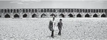  ?? VAHID SALEMI/AP ?? Global warming has taken a toll in Iran, where a woman and a boy walk on a dried up riverbed of the Zayandeh Roud river.