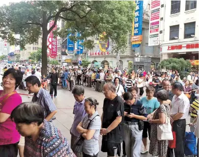  ??  ?? A line of hungry shoppers wait to get mooncakes for Mid-Autumn Festival outside Sunya Cantonese Restaurant at Nanjing Road Pedestrian Mall. Below: At Zhen Laodafang Store a frenzied crowd grab pork mooncakes at the same tourist walking street. — Yu Tingya/Jiang Xiaowei