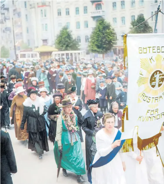  ?? Bild: Hjörnearki­vet ?? Rösträttsd­emonstrati­on i Göteborg den 2 juni 1918. Frigga Carlberg, klädd i svart, är synlig i första ledet efter standarbär­arna. (Bilden är tagen med svartvit film och är färglagd i efterhand av Marina Amaral)