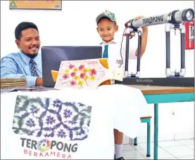  ?? HANUNG HAMBARA/JAWA POS ?? SEPERTI MOTIF BATIK: Fahmi Abidira (kanan) bersama Fajar melihat gambar hasil peneropong­an objek manik-manik yang sudah disimpan di laptop.