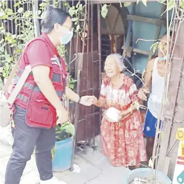  ?? PHOTOGRAPH COURTESY OF PHILIPPINE RED CROSS/FB ?? A VOLUNTEER of the Philippine Red Cross-Caloocan City Chapter greets an elderly during a house visit in Barangay NBBS-Kaunlaran Village in Navotas City. Around 30 senior citizens were treated to hot meals shared by Novotel-Araneta City yesterday, 14 February.