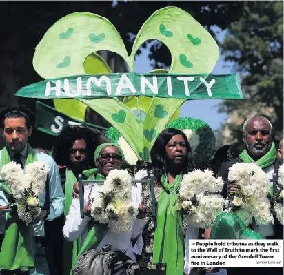  ?? Simon Dawson ?? &gt; People hold tributes as they walk to the Wall of Truth to mark the first anniversar­y of the Grenfell Tower fire in London