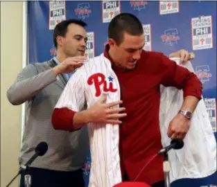  ?? LYNNE SLADKY — THE ASSOCIATED PRESS ?? Phillies general manager Matt Klentak, left, helps catcher J.T. Realmuto put on his new uniform during a news conference at the team’s spring training facility Tuesday in Clearwater, Fla.