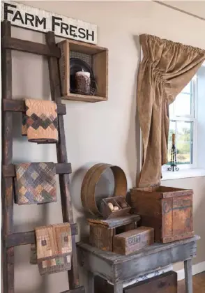  ??  ?? Below: Plucked from a neighbor’s trash, a small table stationed in the dining room now hosts a collection of wooden wares, including a cheese box, egg crate and sifter. The prairie curtains coordinate beautifull­y with an assortment of new quilted squares displayed on a rustic ladder.
Above: Kim recognized this antique spinning wheel’s sculptural qualities and used a ladder, rake and paddle in a dining room wall display to accentuate it.