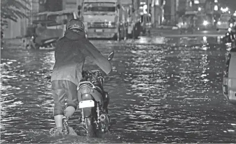  ?? MACKY LIM ?? WATER VS MACHINE. A motorist struggles to push his motorcycle across Monteverde Street in Davao City after it conked out due to the floodwater­s following the heavy downpour Thursday evening.