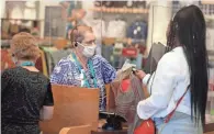  ?? JOURNAL SENTINEL FILES ?? Annie Szczepansk­i, behind a plexiglass shield, checks customers at the Menomonee Falls Kohl's store on May 27, 2020. Kohl's is again asking employees to wear masks in areas where COVID-19 is high.