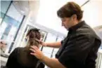  ??  ?? A hairdresse­r uses a socalled tape to attach hair extensions to a woman customer’s natural hair next to the roots.
