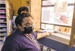  ?? HAYNE PALMOUR IV FOR THE U-T ?? Informatio­n Referral Specialist Anyssa Amaro hands mail Thursday to a man at a window at the Neil Good Day Center in San Diego where clients, who are mostly homeless, can receive services.