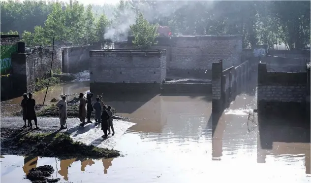  ?? Agence France-presse ?? ↑
Residents stand near the floodwater­s outside their homes in Charsadda district of Khyber Pakhtunkhw­a.