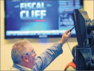  ?? THE ASSOCIATED PRESS ?? James Dresch of MND Partners Inc. works on the floor of the New York Stock Exchange in New York., while a television monitor in the background displays a news report on the “fiscal cliff.”