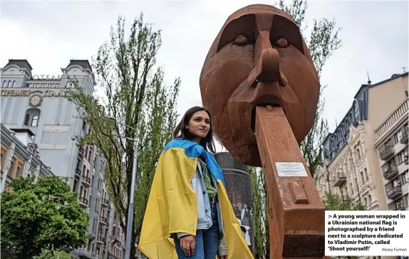  ?? Alexey Furman ?? A young woman wrapped in a Ukrainian national flag is photograph­ed by a friend next to a sculpture dedicated to Vladimir Putin, called ‘Shoot yourself!’