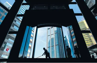  ??  ?? A worker cleans windows at a commercial building in Hong Kong. Authoritie­s say 136 agents recently searched multiple premises in the city.