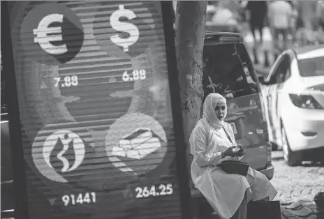  ?? YASIN AKGUL/AFP/GETTY IMAGES ?? A woman sits beside a digital billboard giving updates on various currencies and the Turkish stock exchange in Istanbul on Monday. The record plunge of Turkey’s currency, the lira, has raised concerns of a contagion hitting emerging economies.