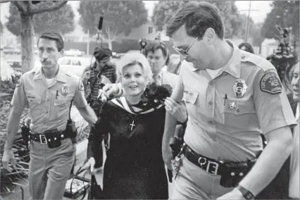  ?? Los Angeles Times ?? ‘SLAP HEARD ’ROUND THE WORLD’ Gabor, being escorted to court, made headlines for her 1989 conviction for assaulting a Beverly Hills police officer. When reporters asked the Hungarian actress, who wed nine times, if she was ready for a long trial, she...