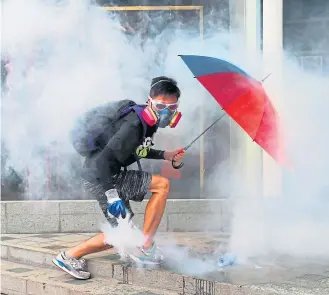  ?? ?? A protester holds an umbrella as he lifts a tear-gas canister fired by police in Hong Kong