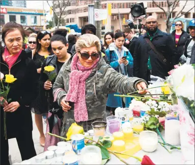  ?? Nathan Denette / Associated Press ?? Ozra Kenari, center, on Tuesday places flowers as she cries at a memorial for the victims along Yonge Street the day after a driver drove a van down sidewalks, striking pedestrian­s in his path, in Toronto.