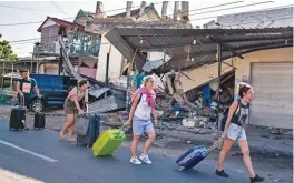  ??  ?? Foreign tourists pulling their suitcases as they walk past damaged buildings following the earthquake.