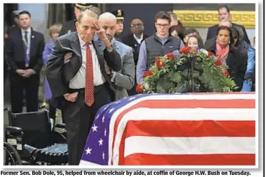  ??  ?? Former Sen. Bob Dole, 95, helped from wheelchair by aide, at coffin of George H.W. Bush on Tuesday.