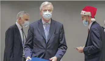  ?? OLIVIER HOSLET, POOL VIA AP ?? A colleague wears a Christmas hat as European Union chief negotiator Michel Barnier ( center) carries a binder of the Brexit trade deal during a special meeting Friday in Brussels.