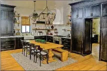  ?? CHRISTOPHE­R OQUENDO/AJC FILE ?? The sprawling kitchen in R. Hardy Smith and Terrie Rice’s Canton home doubles as a breakfast nook with a wooden table, chairs and bench. Black cabinets line the wall and the doorway to the butler’s pantry, and a dramatic white hood hangs over a Thermador range.