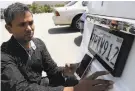  ?? Justin Sullivan / Getty Images ?? Alok Damireddy adjusts a digital license plate in Foster City.