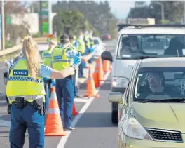  ?? /Bloomberg ?? New cases: Police officers wearing protective masks signal to motorists at a checkpoint in the Bombay area of Auckland, New Zealand, on Wednesday. New Zealand’s world-beating run of being Covid-free has come to an end, with the detection of new cases prompting the government to put the largest city Auckland into lockdown.