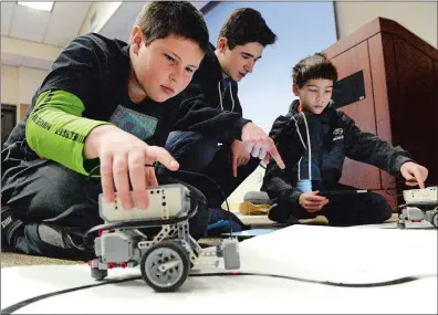  ?? DANA JENSEN THE DAY ?? Kyle Marquardt, 10, places the EV3 Lego robot so its sensor is on the line that it will follow while Aluminum Falcons mentor Connor Hall, center, and Monroe Thomas, 10, right, adjust the speed of the robot so its sensor can see the line more easily during the Encounteri­ng Robots with Aluminum Falcons Robotics & 4-H event Saturday at the Groton Public Library.