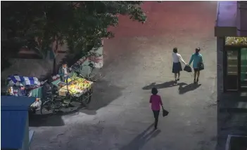  ??  ?? Pedestrian­s passing a fruit vendor through an alleyway in Pyongyang.