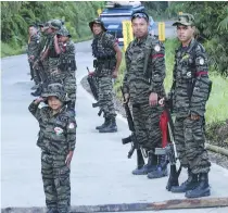  ??  ?? A child in full combat fatigues salutes passersby as rebel fighters from the Moro Islamic Liberation Front (MILF) stand guard by a roadside in southern Mindanao island, Philippine­s.