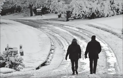  ?? [MIKE STEWART/THE ASSOCIATED PRESS] ?? A couple walks down a snow-covered road Saturday in Kennesaw, Ga. Snowfall shrouding much of the Deep South began tapering off early Saturday, but freezing temperatur­es kept roads slick and thousands without electricit­y while planes remained grounded...