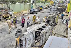  ??  ?? Police and residents walk past charred remains of vehicles vandalised by a mob over a social media post in Bengaluru on Wednesday.