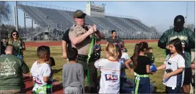  ?? CONTRIBUTE­D PHOTO BY TERESA DOUGLASS ?? Deputy Jason Baillie, center, and Detective Rufino Venegas, right put flags on the players for the first time Jan. 19 as part of the Call of Duty kick-off game for the Sheriff’s new NFL Flag Football League at Groppetti Community Stadium on the campus of Golden West High School in Visalia.