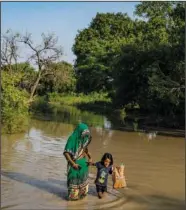  ?? ?? A woman holds the hand of a child and wades through floodwater­s.*