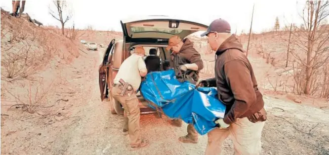  ?? AFP ?? Los oficiales de los condados de Yuba y Butte cargan un cuerpo en un coche fúnebre en Concow, California