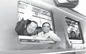  ?? — AFP photo ?? Hun Sen (left) waves beside Prayut as they ride a train during a ceremony to connect the railway line between Cambodia and Thailand in Banteay Meanchey province.