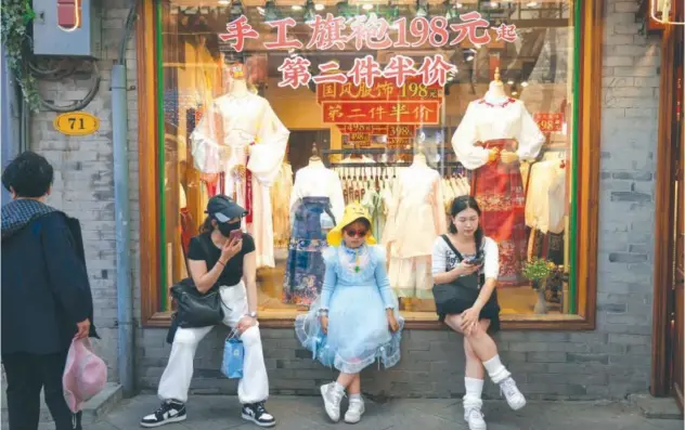  ?? Associated Press ?? ↑
Visitors sit in front of clothing store at the Nanluoguxi­ang, the capital city’s popular tourist spot in Beijing.