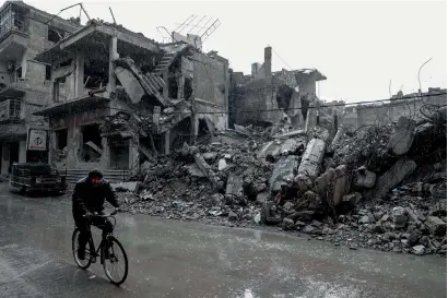  ?? AFP ?? A Syrian man rides his bike under the rain along a damaged street in the rebel-held town of Douma, on the eastern outskirts of Damascus, on Wednesday. —