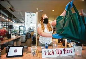  ?? Annie Mulligan / Contributo­r ?? Shannon Beehner hands off a to-go order at the Local Foods location in the Heights. Safety measures put in place for restaurant­s will become standard practice as the Texas economy reopens.