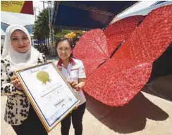  ??  ?? ... Arena Cipta Klasik Sdn Bhd director Asfarena Samion (left) receiving the 'Malaysia Book of Records' certificat­e from its officer Lee Pooi Leng after successful­ly creating the 'biggest hibiscus replica made of beads' at the Malaysia Agro Exposition...